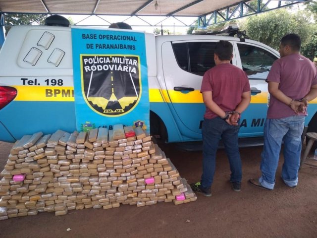 Dupla ao lado dos 300 tabletes de droga que estavam em fundos falsos da camionete. (Foto: Divulgação/PMR)