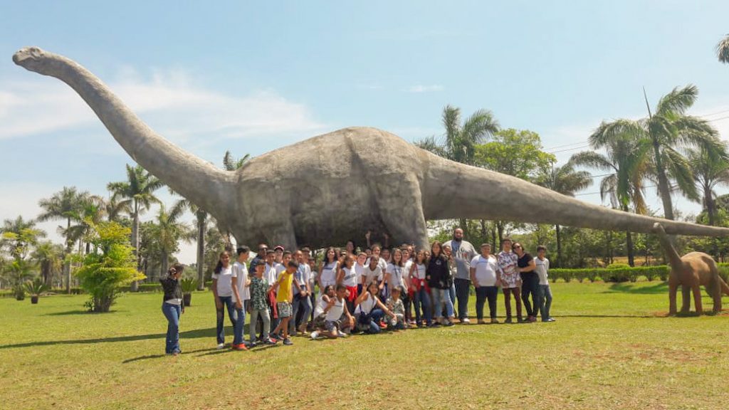 Alunos da Escola Juscelino ao lado da réplica de um titanossauro, um dos maiores animais que já viveram na região do Triângulo Mineiro (Foto: Escola Governador Juscelino)